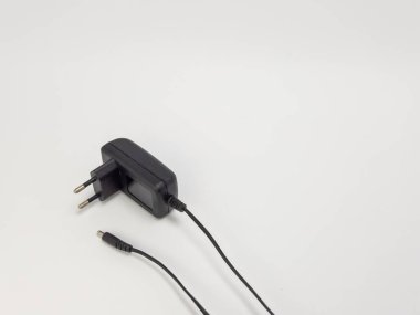 Beyaz arka planda kablo ve fişi olan siyah bir güç adaptörünün yakın plan görüntüsü. Adaptör açılı, fişi ve kablonun sonunu gösteriyor. Görüntü iyi aydınlatılmış, temiz ve basit bir kompozisyonu var. Fotoğraf Ilus için uygun.