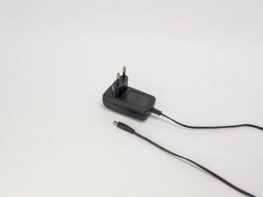 Siyah bir güç adaptörünün yakın çekim görüntüsü. Siyah bir kablo uzanıyor ve sonunda da DC konnektörü. Adaptör beyaz bir yüzeye yerleştirilmiş ve bileşimi basit ve temiz. Görüntü, kurbanın teknik yönünü vurguluyor