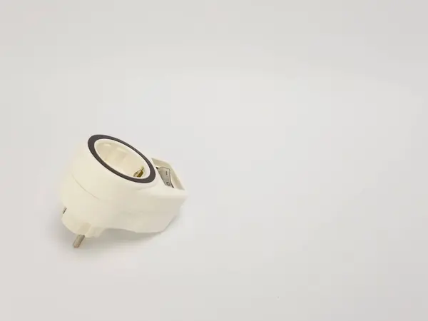Yakın plan bir stüdyo çekimi beyaz bir elektrik adaptörünün iki prizli ve beyaz arka planda bir düğmesi olduğunu gösteriyor. Adaptörün prizlerinden birinin etrafında üç aşamalı bir priz ve siyah bir halka var. Görüntü objeye odaklanarak iyi aydınlatılmış, yüksek.