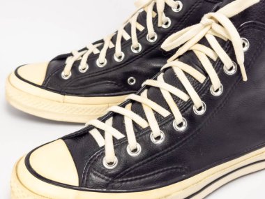 Krem renkli bağcıklı, siyah, yüksek topuklu spor ayakkabıların detaylı bir çekimi. Ayakkabılar beyaz arka plana yerleştiriliyor. Derinin dokusuna, bağcıkların tasarımına ve ayakkabının genel estetiğine odaklanıyor.. 