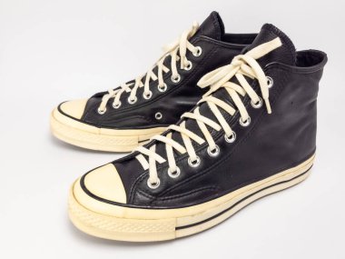 Krem renkli bağcıklı, siyah, yüksek topuklu spor ayakkabıların detaylı bir çekimi. Ayakkabılar beyaz arka plana yerleştiriliyor. Derinin dokusuna, bağcıkların tasarımına ve ayakkabının genel estetiğine odaklanıyor.. 