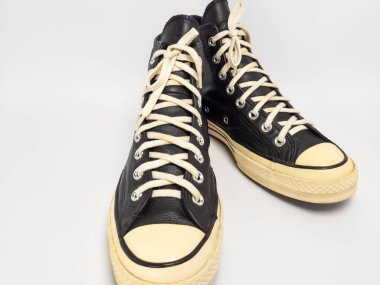 Krem renkli bağcıklı, siyah, yüksek topuklu spor ayakkabıların detaylı bir çekimi. Ayakkabılar beyaz arka plana yerleştiriliyor. Derinin dokusuna, bağcıkların tasarımına ve ayakkabının genel estetiğine odaklanıyor.. 