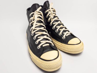 Krem renkli bağcıklı, siyah, yüksek topuklu spor ayakkabıların detaylı bir çekimi. Ayakkabılar beyaz arka plana yerleştiriliyor. Derinin dokusuna, bağcıkların tasarımına ve ayakkabının genel estetiğine odaklanıyor.. 