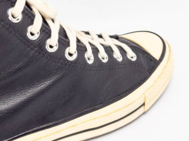 Krem renkli bağcıklı, siyah, yüksek topuklu spor ayakkabıların detaylı bir çekimi. Ayakkabılar beyaz arka plana yerleştiriliyor. Derinin dokusuna, bağcıkların tasarımına ve ayakkabının genel estetiğine odaklanıyor.. 