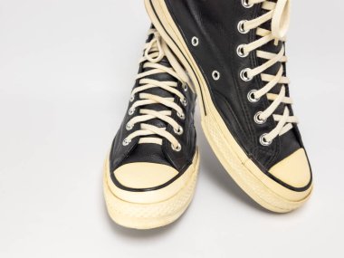 Krem renkli bağcıklı, siyah, yüksek topuklu spor ayakkabıların detaylı bir çekimi. Ayakkabılar beyaz arka plana yerleştiriliyor. Derinin dokusuna, bağcıkların tasarımına ve ayakkabının genel estetiğine odaklanıyor.. 