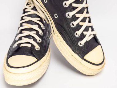 Krem renkli bağcıklı, siyah, yüksek topuklu spor ayakkabıların detaylı bir çekimi. Ayakkabılar beyaz arka plana yerleştiriliyor. Derinin dokusuna, bağcıkların tasarımına ve ayakkabının genel estetiğine odaklanıyor.. 