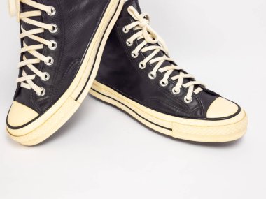 Krem renkli bağcıklı, siyah, yüksek topuklu spor ayakkabıların detaylı bir çekimi. Ayakkabılar beyaz arka plana yerleştiriliyor. Derinin dokusuna, bağcıkların tasarımına ve ayakkabının genel estetiğine odaklanıyor.. 