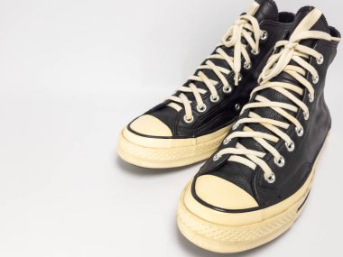 Krem renkli bağcıklı, siyah, yüksek topuklu spor ayakkabıların detaylı bir çekimi. Ayakkabılar beyaz arka plana yerleştiriliyor. Derinin dokusuna, bağcıkların tasarımına ve ayakkabının genel estetiğine odaklanıyor.. 