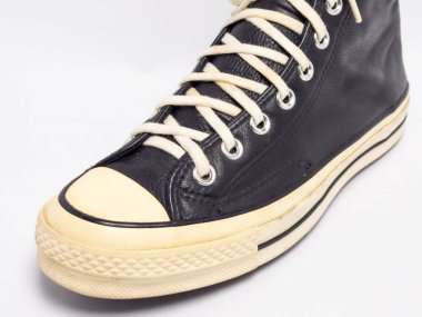 Krem renkli bağcıklı, siyah, yüksek topuklu spor ayakkabıların detaylı bir çekimi. Ayakkabılar beyaz arka plana yerleştiriliyor. Derinin dokusuna, bağcıkların tasarımına ve ayakkabının genel estetiğine odaklanıyor.. 