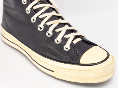 Krem renkli bağcıklı, siyah, yüksek topuklu spor ayakkabıların detaylı bir çekimi. Ayakkabılar beyaz arka plana yerleştiriliyor. Derinin dokusuna, bağcıkların tasarımına ve ayakkabının genel estetiğine odaklanıyor.. 