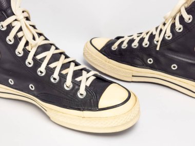 Krem renkli bağcıklı, siyah, yüksek topuklu spor ayakkabıların detaylı bir çekimi. Ayakkabılar beyaz arka plana yerleştiriliyor. Derinin dokusuna, bağcıkların tasarımına ve ayakkabının genel estetiğine odaklanıyor.. 