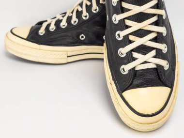 Krem renkli bağcıklı, siyah, yüksek topuklu spor ayakkabıların detaylı bir çekimi. Ayakkabılar beyaz arka plana yerleştiriliyor. Derinin dokusuna, bağcıkların tasarımına ve ayakkabının genel estetiğine odaklanıyor.. 