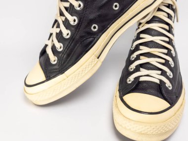 Krem renkli bağcıklı, siyah, yüksek topuklu spor ayakkabıların detaylı bir çekimi. Ayakkabılar beyaz arka plana yerleştiriliyor. Derinin dokusuna, bağcıkların tasarımına ve ayakkabının genel estetiğine odaklanıyor.. 