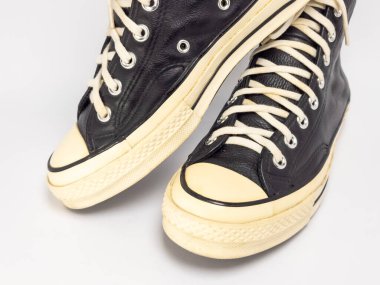 Krem renkli bağcıklı, siyah, yüksek topuklu spor ayakkabıların detaylı bir çekimi. Ayakkabılar beyaz arka plana yerleştiriliyor. Derinin dokusuna, bağcıkların tasarımına ve ayakkabının genel estetiğine odaklanıyor.. 