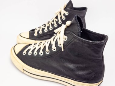 Krem renkli bağcıklı, siyah, yüksek topuklu spor ayakkabıların detaylı bir çekimi. Ayakkabılar beyaz arka plana yerleştiriliyor. Derinin dokusuna, bağcıkların tasarımına ve ayakkabının genel estetiğine odaklanıyor.. 