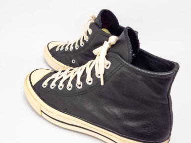 Krem renkli bağcıklı, siyah, yüksek topuklu spor ayakkabıların detaylı bir çekimi. Ayakkabılar beyaz arka plana yerleştiriliyor. Derinin dokusuna, bağcıkların tasarımına ve ayakkabının genel estetiğine odaklanıyor.. 