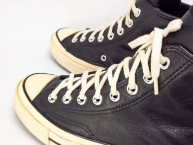 Krem renkli bağcıklı, siyah, yüksek topuklu spor ayakkabıların detaylı bir çekimi. Ayakkabılar beyaz arka plana yerleştiriliyor. Derinin dokusuna, bağcıkların tasarımına ve ayakkabının genel estetiğine odaklanıyor.. 