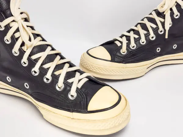 Krem renkli bağcıklı, siyah, yüksek topuklu spor ayakkabıların detaylı bir çekimi. Ayakkabılar beyaz arka plana yerleştiriliyor. Derinin dokusuna, bağcıkların tasarımına ve ayakkabının genel estetiğine odaklanıyor.. 