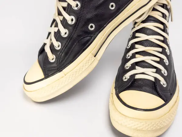 Krem renkli bağcıklı, siyah, yüksek topuklu spor ayakkabıların detaylı bir çekimi. Ayakkabılar beyaz arka plana yerleştiriliyor. Derinin dokusuna, bağcıkların tasarımına ve ayakkabının genel estetiğine odaklanıyor.. 