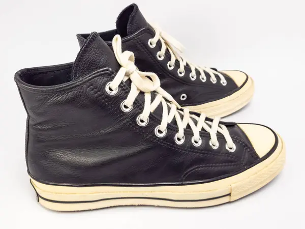 Krem renkli bağcıklı, siyah, yüksek topuklu spor ayakkabıların detaylı bir çekimi. Ayakkabılar beyaz arka plana yerleştiriliyor. Derinin dokusuna, bağcıkların tasarımına ve ayakkabının genel estetiğine odaklanıyor.. 