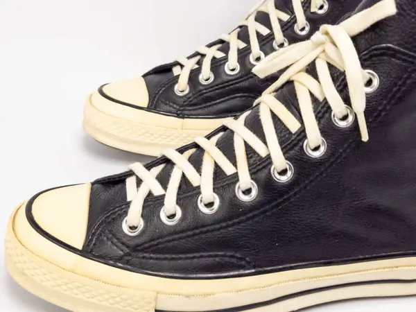 Krem renkli bağcıklı, siyah, yüksek topuklu spor ayakkabıların detaylı bir çekimi. Ayakkabılar beyaz arka plana yerleştiriliyor. Derinin dokusuna, bağcıkların tasarımına ve ayakkabının genel estetiğine odaklanıyor.. 