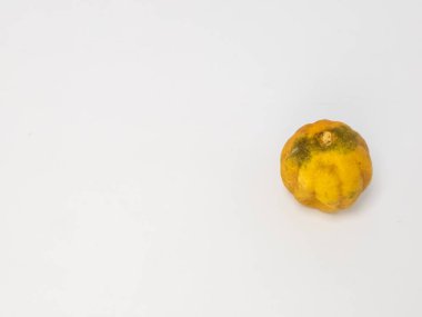 Bu resim, buruşuk, sarı turunçgil meyvesinin, muhtemelen limon ya da benzeri bir meyvenin, temiz, sade beyaz bir arka planda yakın plan görüntüsünü içerir. Meyvenin dokusu ve rengi eski ya da biraz çürümüş olabileceğini gösteriyor..