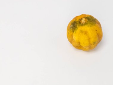 Bu resim, buruşuk, sarı turunçgil meyvesinin, muhtemelen limon ya da benzeri bir meyvenin, temiz, sade beyaz bir arka planda yakın plan görüntüsünü içerir. Meyvenin dokusu ve rengi eski ya da biraz çürümüş olabileceğini gösteriyor..