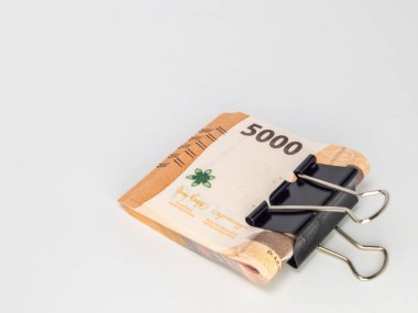 Siyah bir klasör klibiyle tutturulmuş Endonezya Rupiah banknotlarının yer aldığı yakın plan bir fotoğraf. Banknotlar odaklı ve arka plan bembeyaz. Görüntü para, tasarruf ve para gibi finansal kavramları iletir.