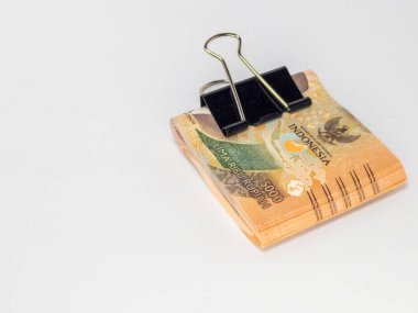 Siyah bir klasör klibiyle tutturulmuş Endonezya Rupiah banknotlarının yer aldığı yakın plan bir fotoğraf. Banknotlar odaklı ve arka plan bembeyaz. Görüntü para, tasarruf ve para gibi finansal kavramları iletir.