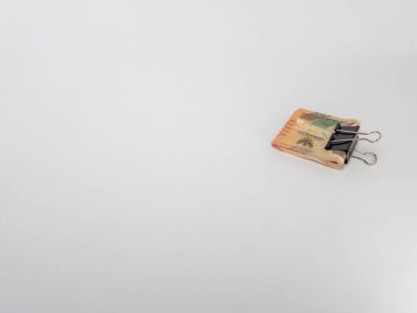 Siyah bir klasör klibiyle tutturulmuş Endonezya Rupiah banknotlarının yer aldığı yakın plan bir fotoğraf. Banknotlar odaklı ve arka plan bembeyaz. Görüntü para, tasarruf ve para gibi finansal kavramları iletir.