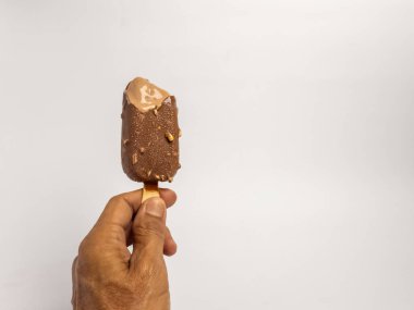 Kısmen yenmiş çikolatalı dondurmayı fındıklı tutarken çekilmiş yakın plan bir fotoğraf. Dondurma hafifçe eriyor ve arka plan bembeyaz. Görüntüde basit bir kompozisyon var, ana konu olarak dondurmaya odaklanıyor..