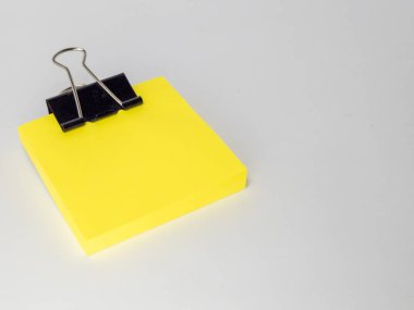 Siyah bir klasör klipsiyle tutturulmuş parlak sarı yapışkan banknotların yakın çekim çekimi. Notlar düz, açık gri bir yüzeye yerleştirilmiş. Bu da negatif alan yaratıyor..