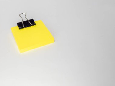 Siyah bir klasör klipsiyle tutturulmuş parlak sarı yapışkan banknotların yakın çekim çekimi. Notlar düz, açık gri bir yüzeye yerleştirilmiş. Bu da negatif alan yaratıyor..