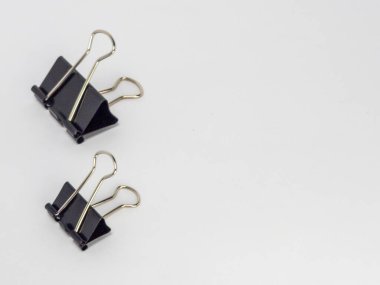 Bu resim, temiz beyaz arkaplana karşı hafif bir açıyla yerleştirilmiş iki siyah klasör klipsi içerir. Ana odak noktaları kliplerdir, tasarımlarını ve metal saplarının etkileşimini gösterirler..