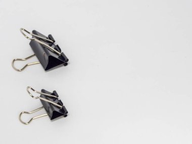 Bu resim, temiz beyaz arkaplana karşı hafif bir açıyla yerleştirilmiş iki siyah klasör klipsi içerir. Ana odak noktaları kliplerdir, tasarımlarını ve metal saplarının etkileşimini gösterirler..
