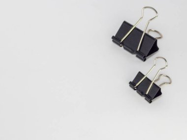 Bu resim, temiz beyaz arkaplana karşı hafif bir açıyla yerleştirilmiş iki siyah klasör klipsi içerir. Ana odak noktaları kliplerdir, tasarımlarını ve metal saplarının etkileşimini gösterirler..