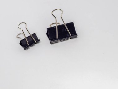 Bu resim, temiz beyaz arkaplana karşı hafif bir açıyla yerleştirilmiş iki siyah klasör klipsi içerir. Ana odak noktaları kliplerdir, tasarımlarını ve metal saplarının etkileşimini gösterirler..