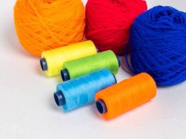 Kırmızı, mavi, sarı, yeşil ve turuncu da dahil olmak üzere çeşitli iplik makaraları ve topları içeren canlı bir kompozisyon. Renkli makaralar, daha büyük iplik toplarının yanına dizilmiştir, hepsi temiz beyaz arka plana karşıdır..