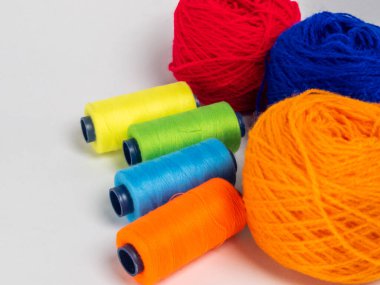 Kırmızı, mavi, sarı, yeşil ve turuncu da dahil olmak üzere çeşitli iplik makaraları ve topları içeren canlı bir kompozisyon. Renkli makaralar, daha büyük iplik toplarının yanına dizilmiştir, hepsi temiz beyaz arka plana karşıdır..