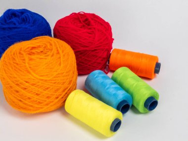 Kırmızı, mavi, sarı, yeşil ve turuncu da dahil olmak üzere çeşitli iplik makaraları ve topları içeren canlı bir kompozisyon. Renkli makaralar, daha büyük iplik toplarının yanına dizilmiştir, hepsi temiz beyaz arka plana karşıdır..