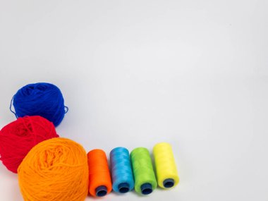 Kırmızı, mavi, sarı, yeşil ve turuncu da dahil olmak üzere çeşitli iplik makaraları ve topları içeren canlı bir kompozisyon. Renkli makaralar, daha büyük iplik toplarının yanına dizilmiştir, hepsi temiz beyaz arka plana karşıdır..