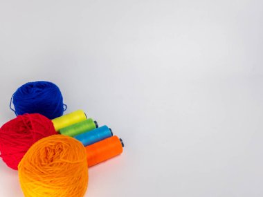 Kırmızı, mavi, sarı, yeşil ve turuncu da dahil olmak üzere çeşitli iplik makaraları ve topları içeren canlı bir kompozisyon. Renkli makaralar, daha büyük iplik toplarının yanına dizilmiştir, hepsi temiz beyaz arka plana karşıdır..