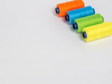 Resim dört iplik makarasına canlı renkte sahiptir: turuncu, yeşil, mavi ve sarı. Çapraz olarak temiz beyaz bir arkaplanda dizilmişler. Spikerler koyu mavi çekirdekli silindirik..