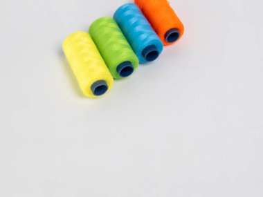 Resim dört iplik makarasına canlı renkte sahiptir: turuncu, yeşil, mavi ve sarı. Çapraz olarak temiz beyaz bir arkaplanda dizilmişler. Spikerler koyu mavi çekirdekli silindirik..