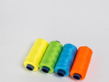 Resim dört iplik makarasına canlı renkte sahiptir: turuncu, yeşil, mavi ve sarı. Çapraz olarak temiz beyaz bir arkaplanda dizilmişler. Spikerler koyu mavi çekirdekli silindirik..