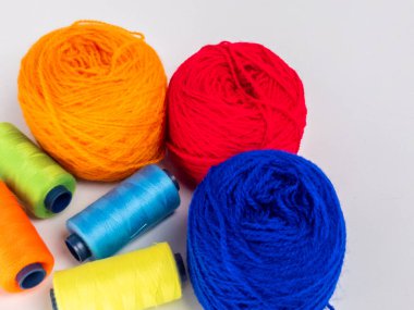 Kırmızı, mavi, sarı, yeşil ve turuncu da dahil olmak üzere çeşitli iplik makaraları ve topları içeren canlı bir kompozisyon. Renkli makaralar, daha büyük iplik toplarının yanına dizilmiştir, hepsi temiz beyaz arka plana karşıdır..