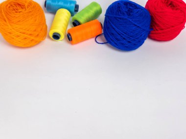 Kırmızı, mavi, sarı, yeşil ve turuncu da dahil olmak üzere çeşitli iplik makaraları ve topları içeren canlı bir kompozisyon. Renkli makaralar, daha büyük iplik toplarının yanına dizilmiştir, hepsi temiz beyaz arka plana karşıdır..