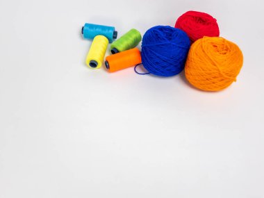 Kırmızı, mavi, sarı, yeşil ve turuncu da dahil olmak üzere çeşitli iplik makaraları ve topları içeren canlı bir kompozisyon. Renkli makaralar, daha büyük iplik toplarının yanına dizilmiştir, hepsi temiz beyaz arka plana karşıdır..
