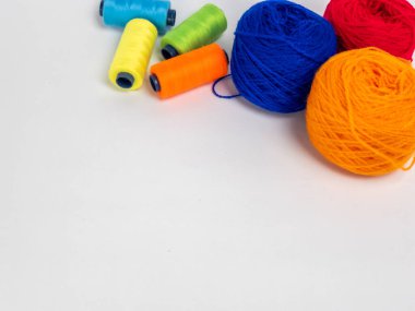 Kırmızı, mavi, sarı, yeşil ve turuncu da dahil olmak üzere çeşitli iplik makaraları ve topları içeren canlı bir kompozisyon. Renkli makaralar, daha büyük iplik toplarının yanına dizilmiştir, hepsi temiz beyaz arka plana karşıdır..