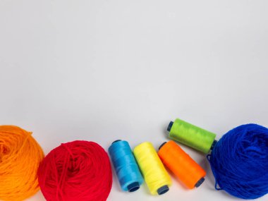 Kırmızı, mavi, sarı, yeşil ve turuncu da dahil olmak üzere çeşitli iplik makaraları ve topları içeren canlı bir kompozisyon. Renkli makaralar, daha büyük iplik toplarının yanına dizilmiştir, hepsi temiz beyaz arka plana karşıdır..